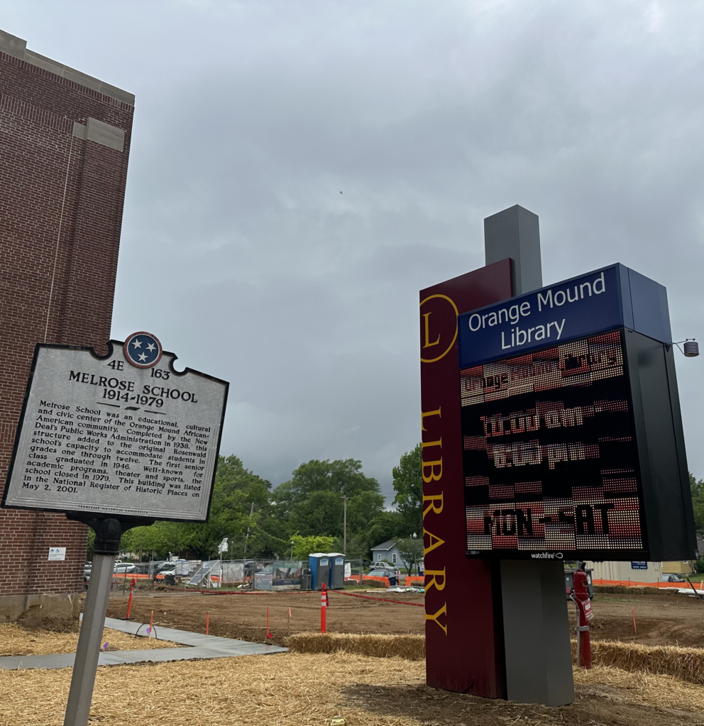 A historical marker for Melrose High School next to an electronic sign displaying hours for the Orange Mound Library, with construction ongoing in the background, featured in Memphis News.