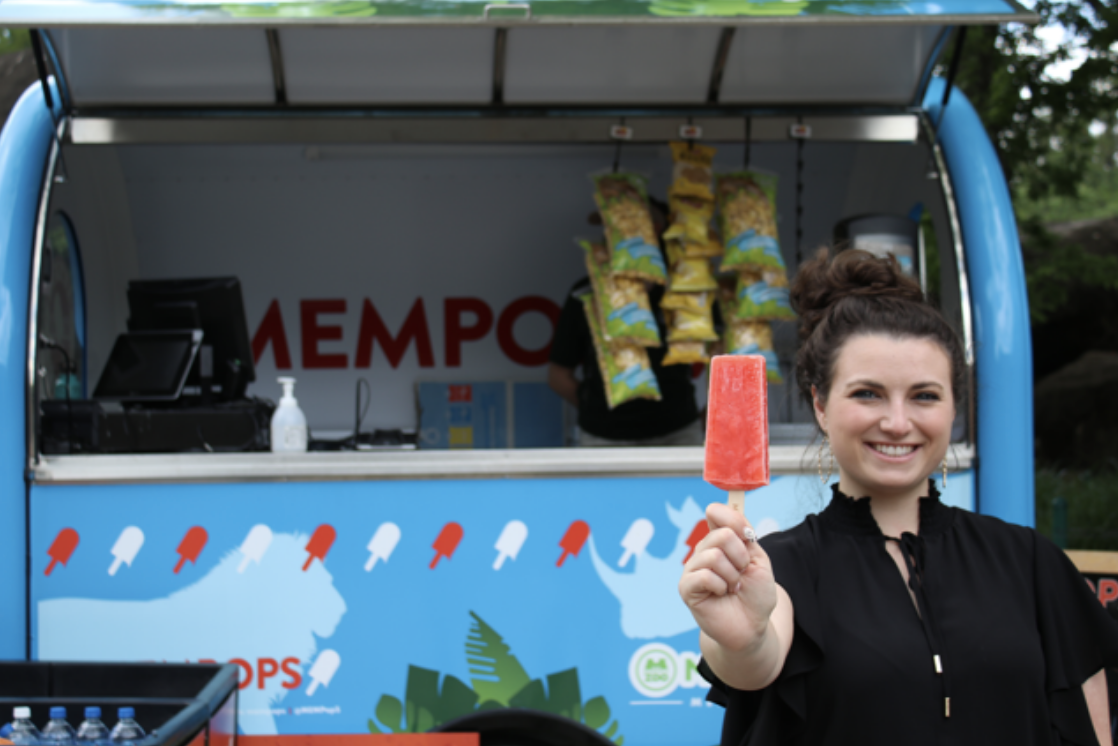 Woman smiling and holding a red popsicle in front of a blue ice cream truck with visible brand "mempops", one of the popular ice cream shops in Memphis.