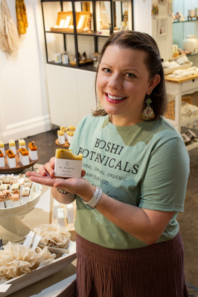 A woman in a sustainable botanical shop holding a product and smiling at the camera.