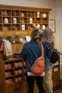 Two people looking at sustainable products on wooden shelves in a store, one person reaching for an item on a higher shelf.