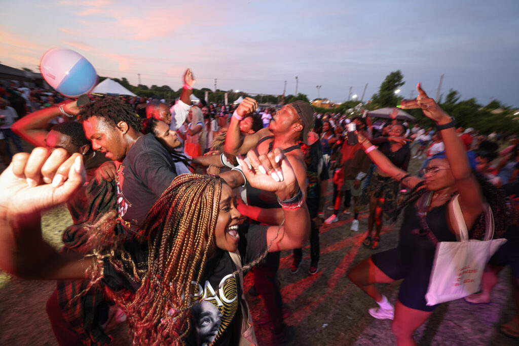Crowd of joyful people celebrating at the Juneteenth Festival during sunset, dancing and raising their hands in the air.