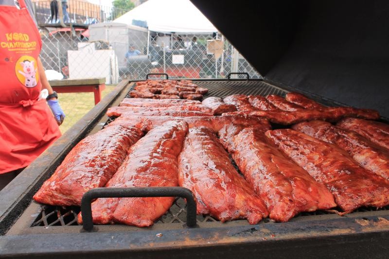 Grilled ribs at the Memphis BBQ Fest with a chef in a red apron at an outdoor event.